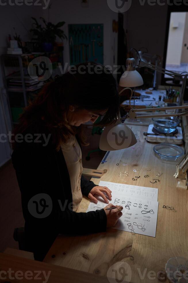Female master painting jewelry sketches in dark workshop photo