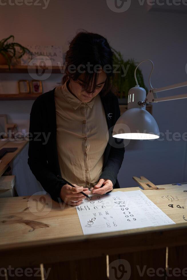 Focused female jeweler with ring and sketches at table photo