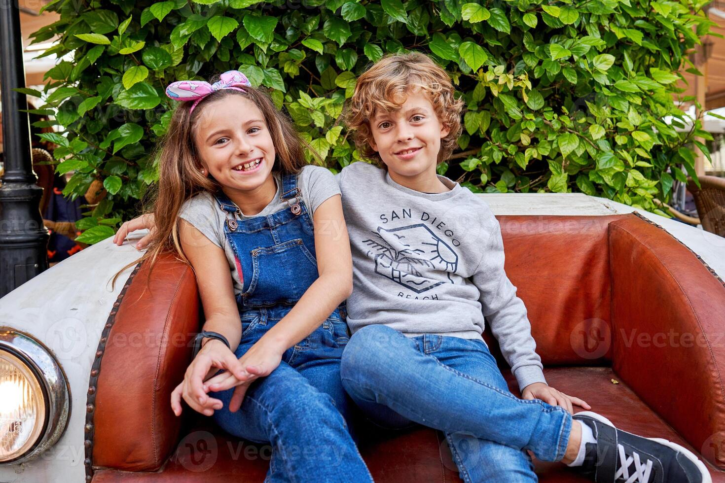 Cheerful boy and girl sitting on leather sofa in garden photo
