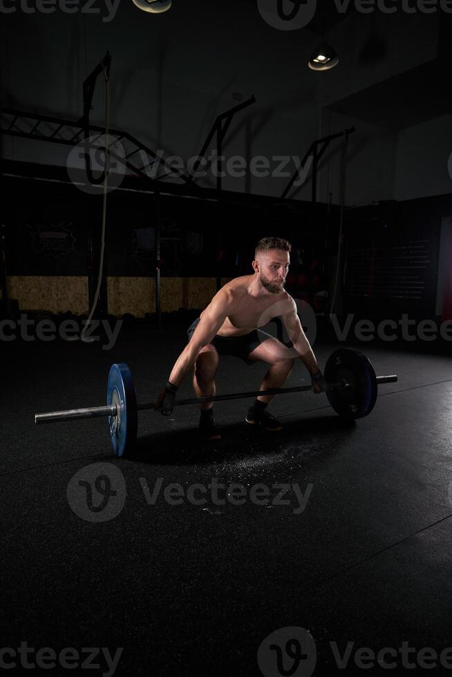 Young strong sportsman doing exercises with barbell with weights photo