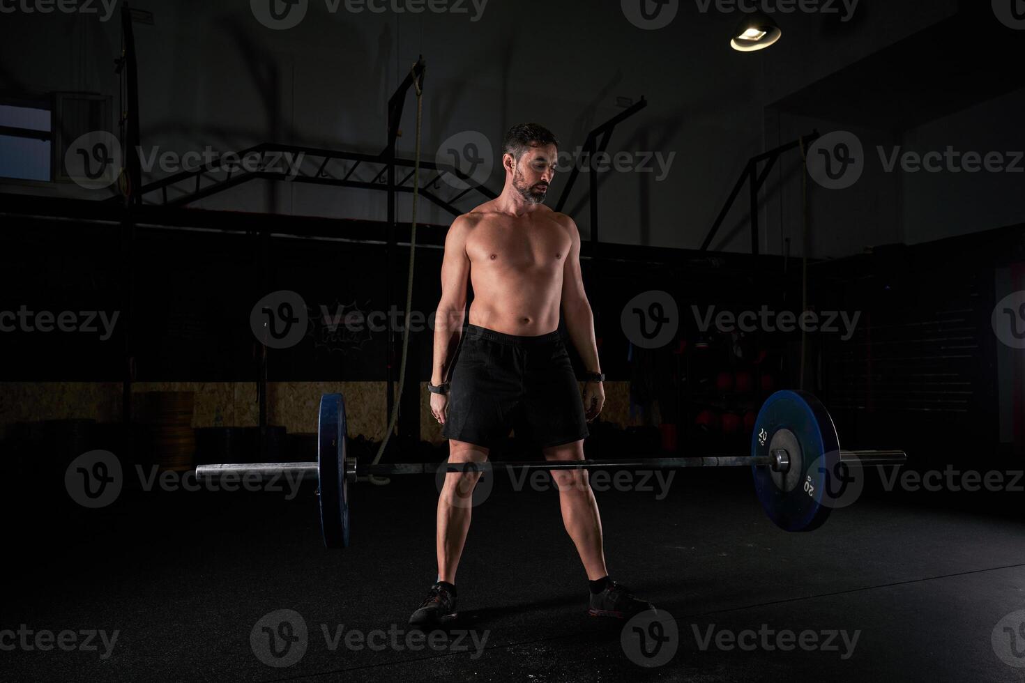Muscular strong man preparing for lifting barbell with weights photo
