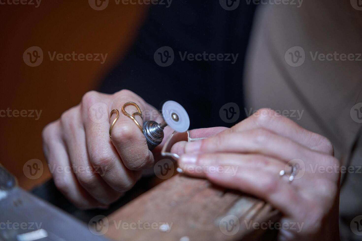 Crop anonymous jeweler using polisher during work at bench photo