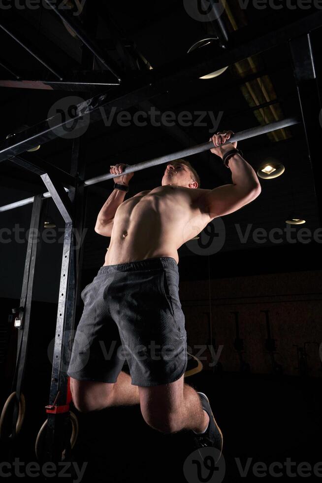 Shirtless sportsman performing exercise on bar photo