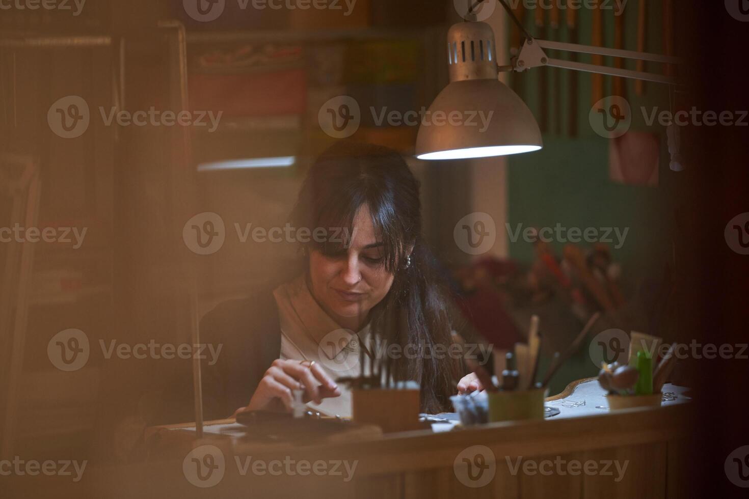 Focused ethnic female jeweler checking new created accessories photo