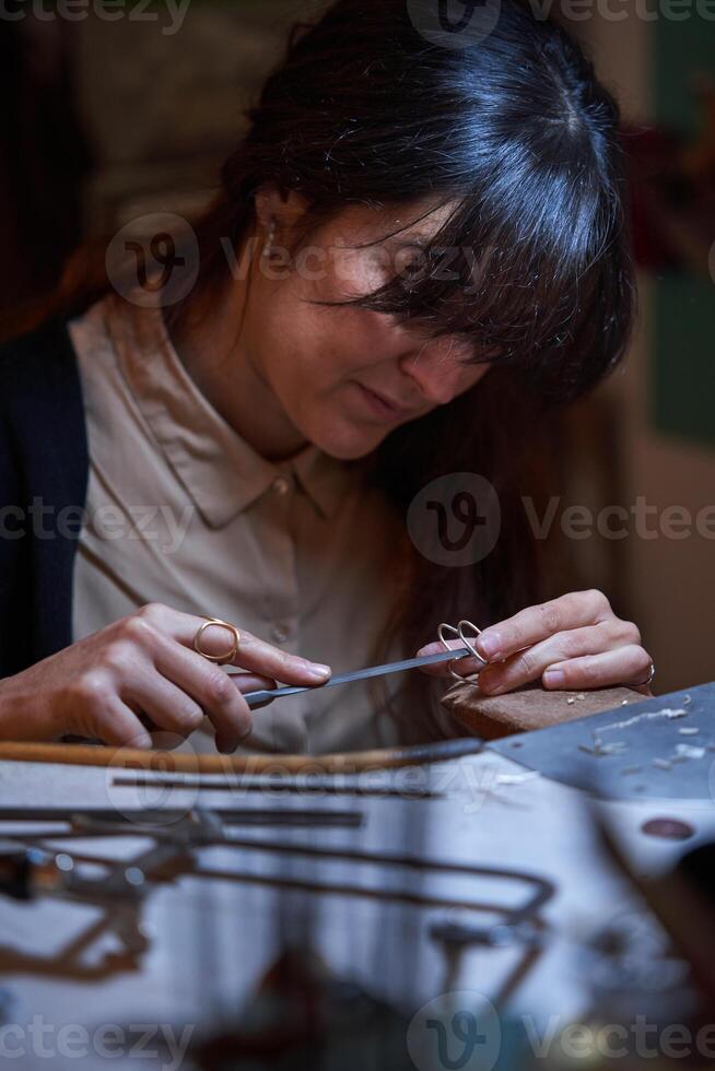 Attentive ethnic craftswoman using flat file while creating jewe photo