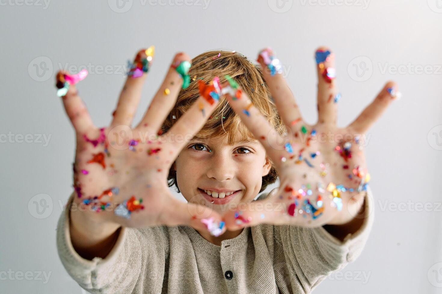 Positive kid showing hands with colorful confetti during party photo