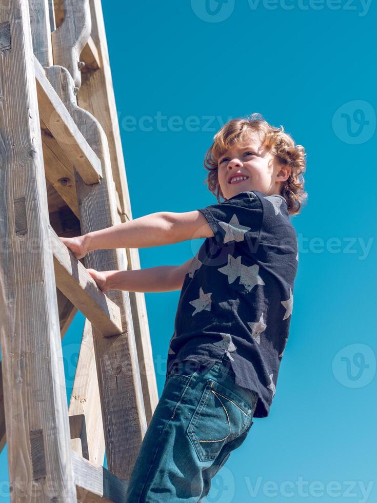 Delightful child standing on wooden ladder of playground photo