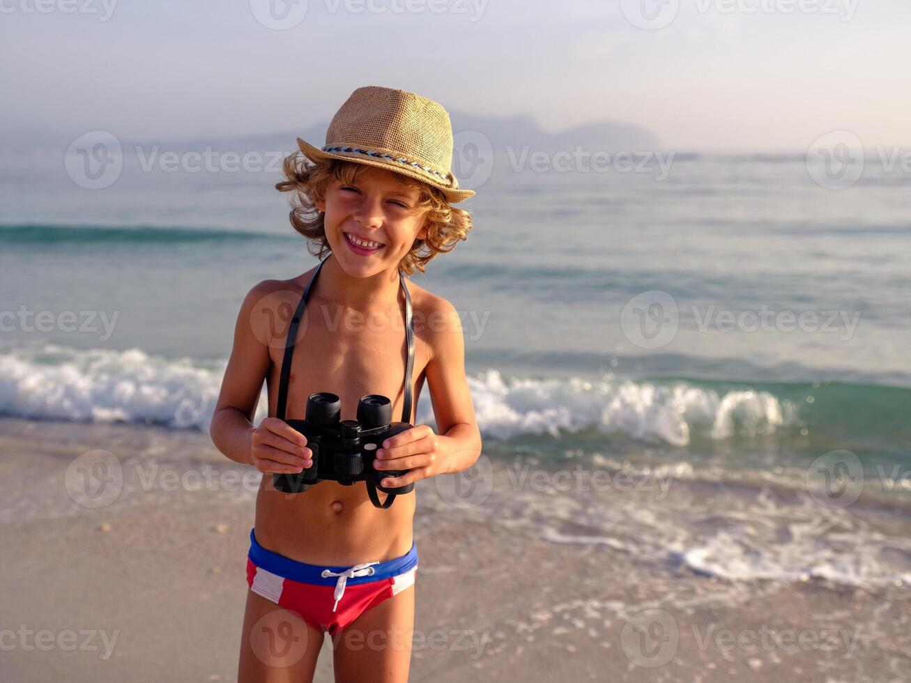 Smiling boy with binoculars standing on sandy beach photo