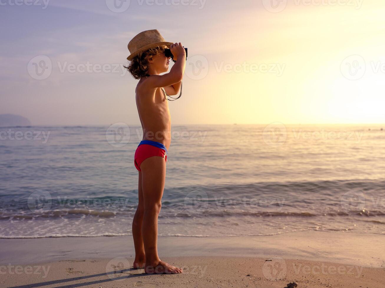 Boy observing sea from binoculars at sunset photo