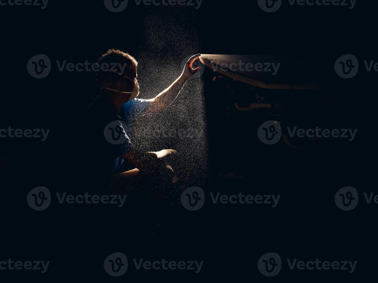 Man checking smoothness of surfboard in dark workshop photo