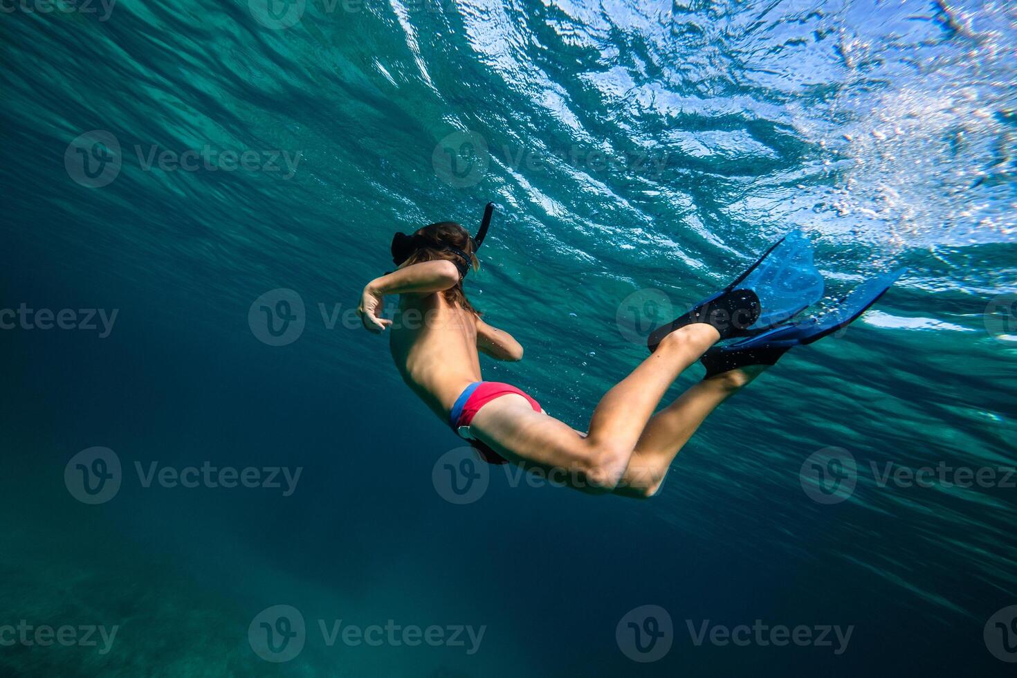 Teenager in diving mask and flippers swimming underwater in sea photo