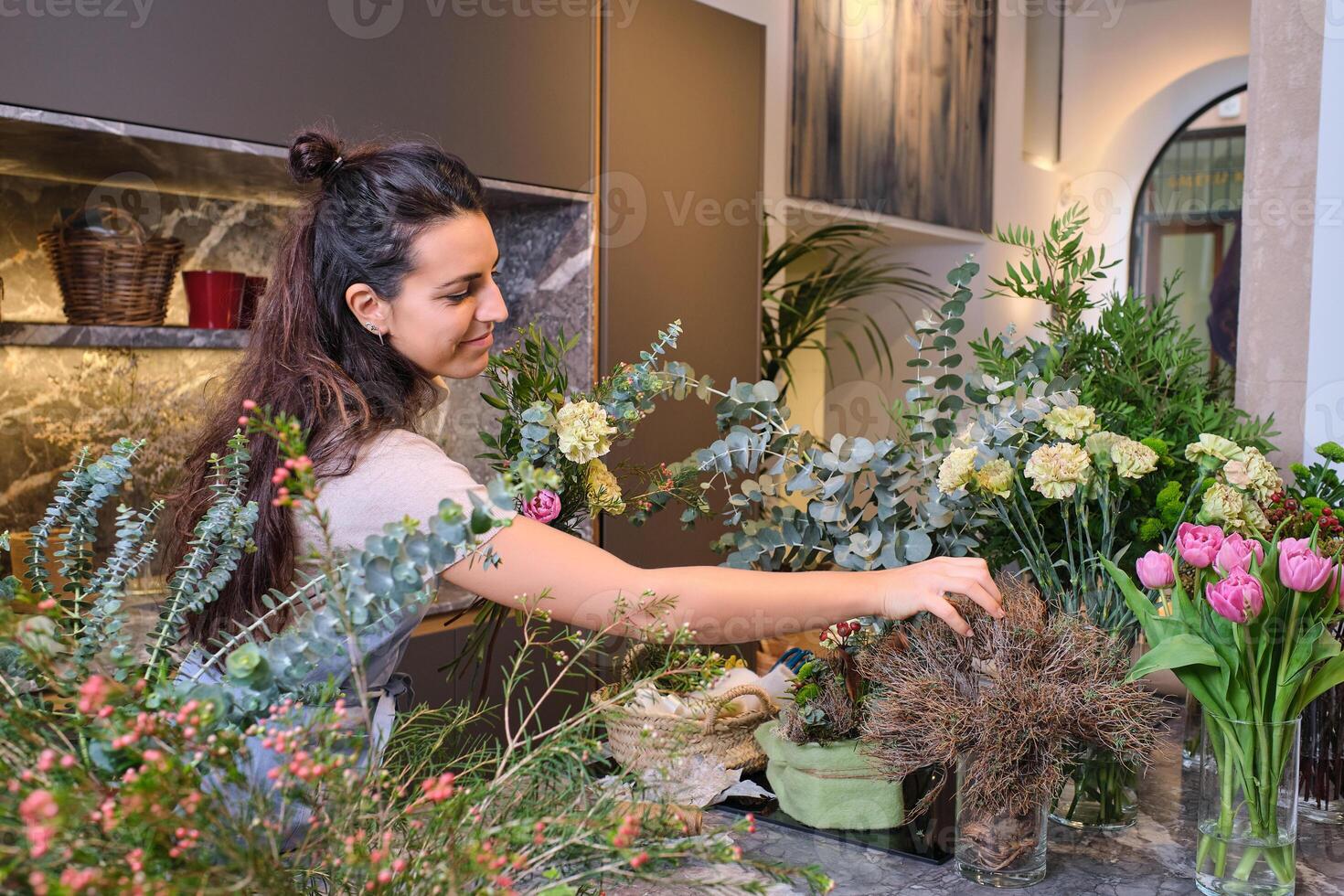Young woman standing at table with various blooming flowers in f photo