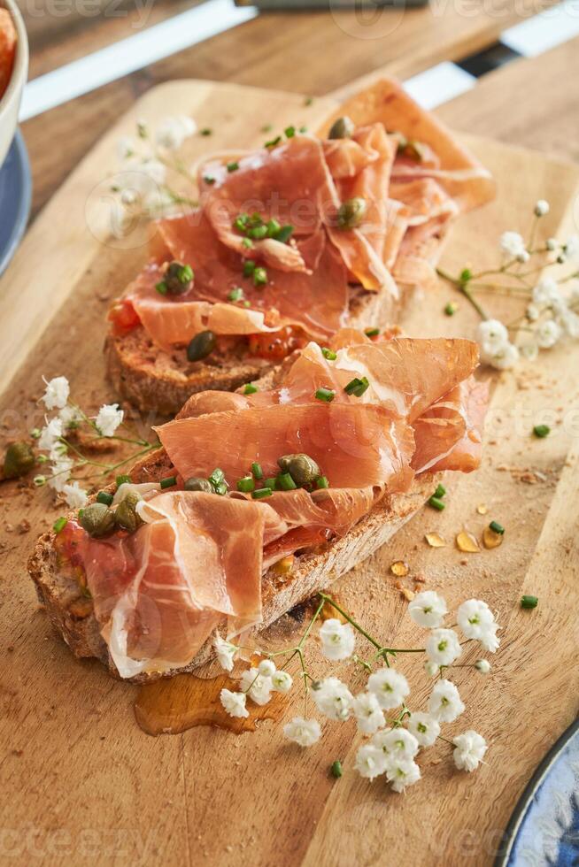Delicious bruschettas with prosciutto and capers served on wooden board photo