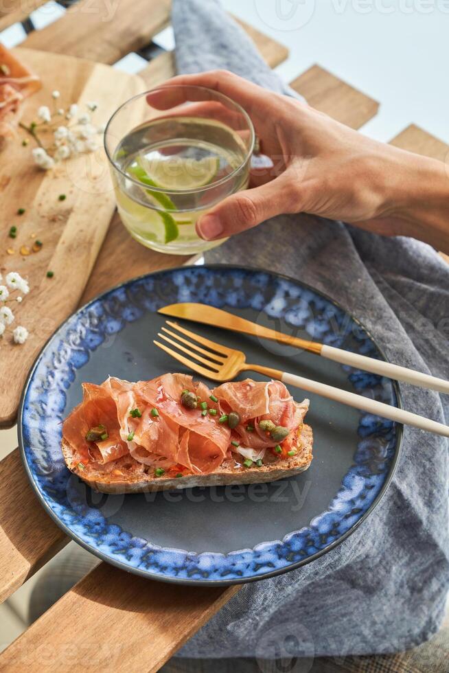 Anonymous person having breakfast with prosciutto toast and lime water on terrace photo