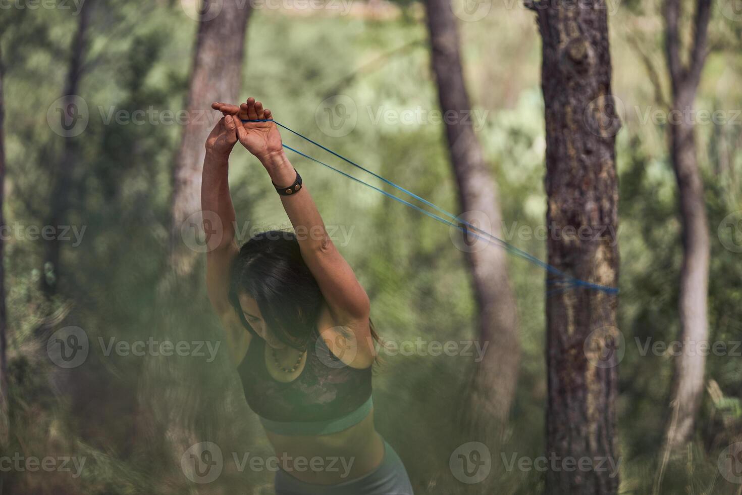 Woman stretching resistance band during training in forest photo