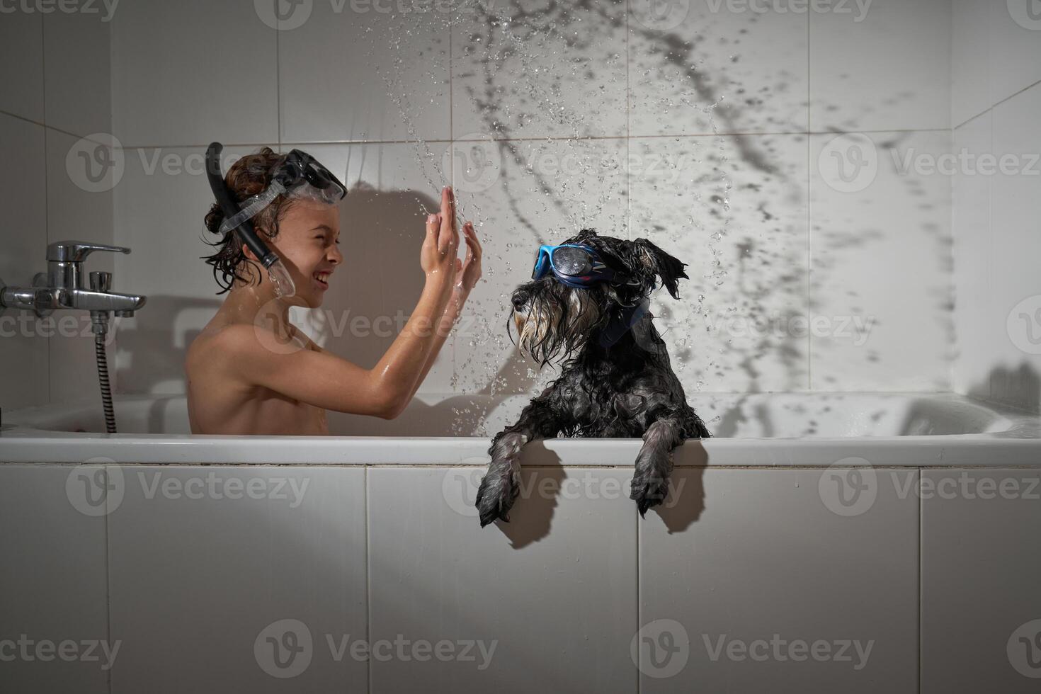 Smiling boy splashing water in tub with dog photo