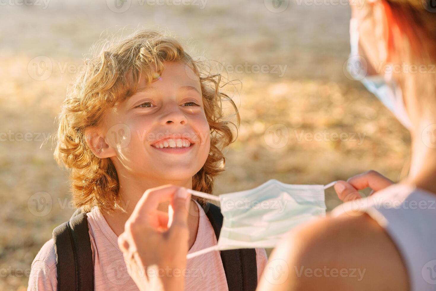 Unrecognizable woman putting mask on cheerful boy photo