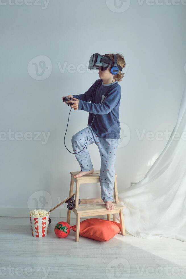 Curious boy in VR glasses and headphones playing with joystick photo