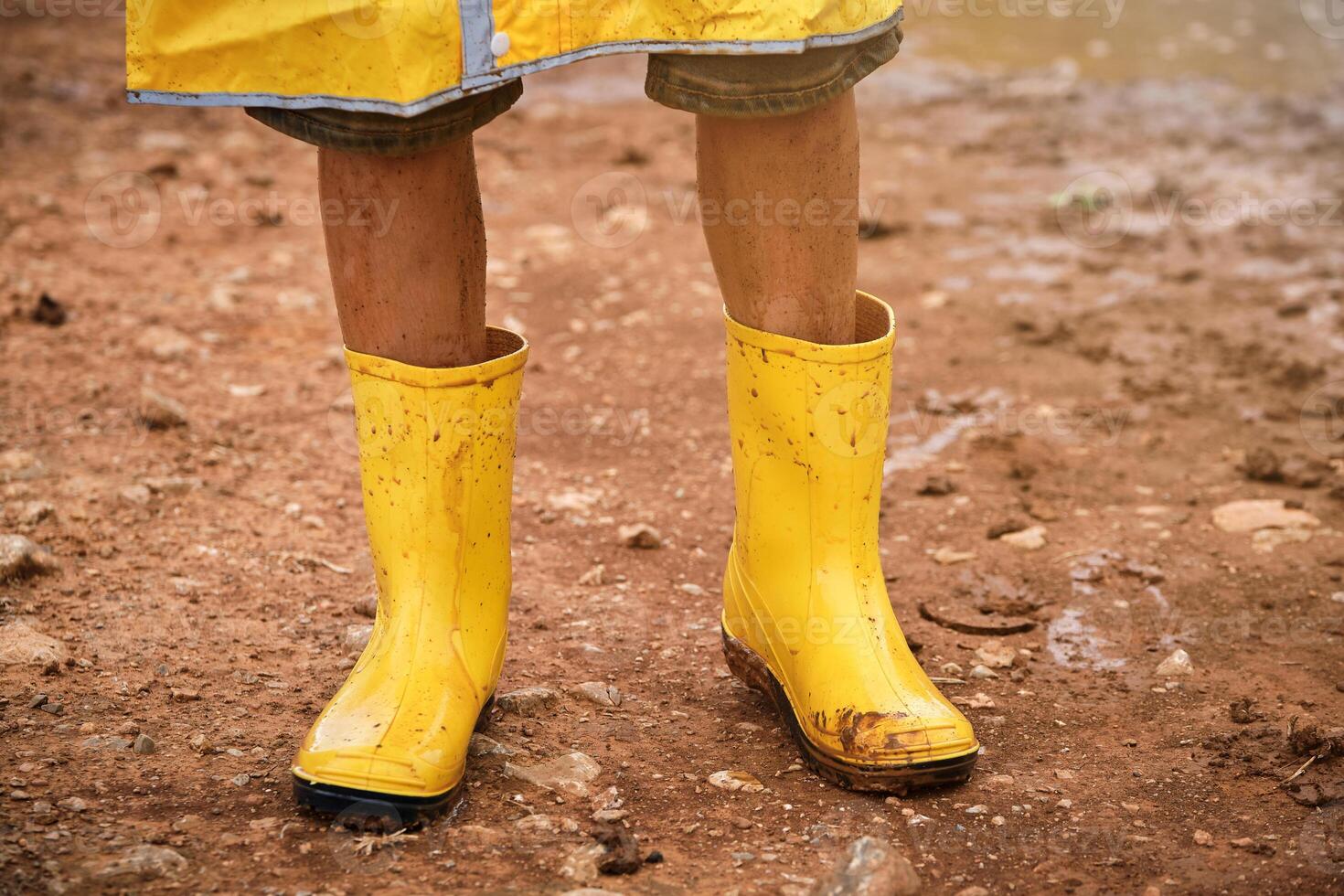Crop child wearing yellow raincoat and standing in mud photo