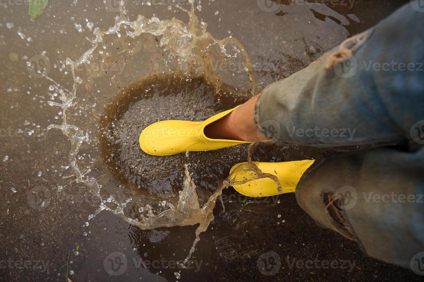 Crop person in rubber boots playing in puddle photo