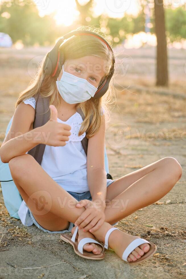 Girl in mask sitting on ground and showing thumb up photo