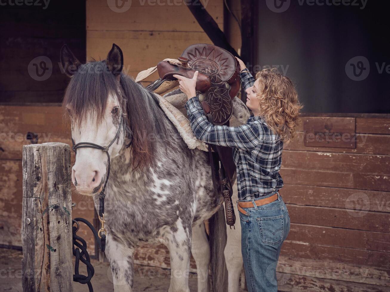 Woman putting on saddle on horse photo