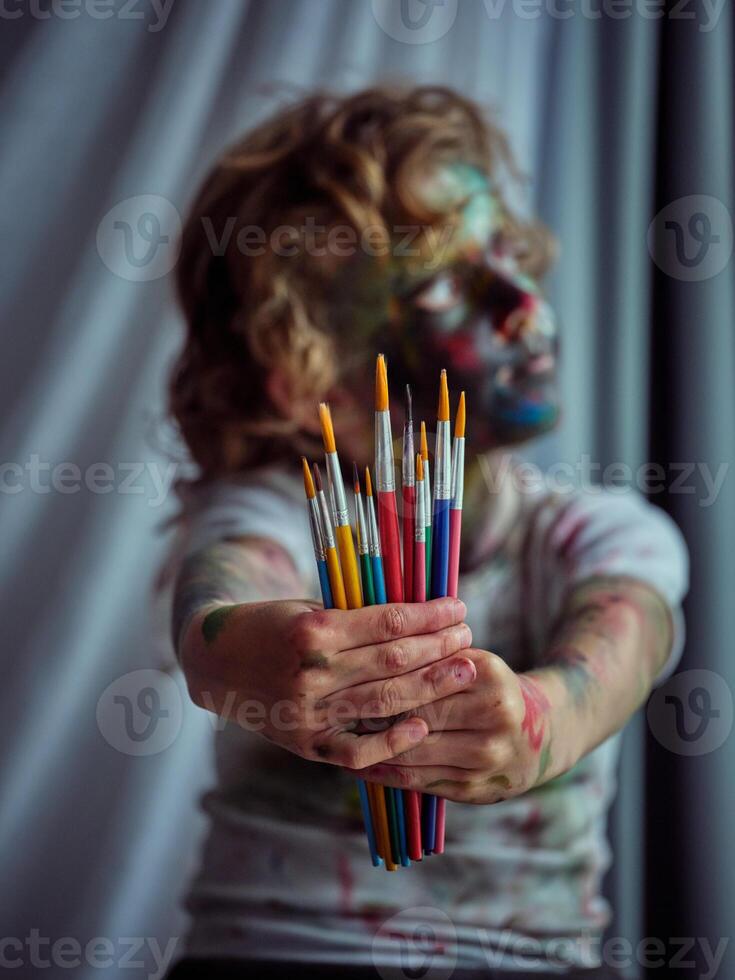 Messy boy showing set of paintbrushes photo