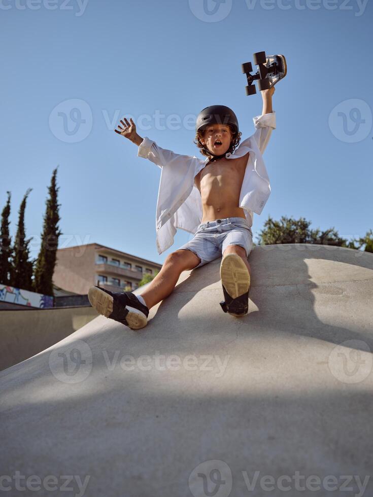 Excited boy with skateboard sitting on ramp photo
