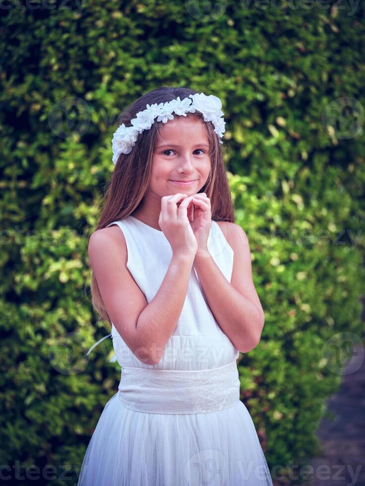 Smiling girl in flower wreath standing against green trees photo