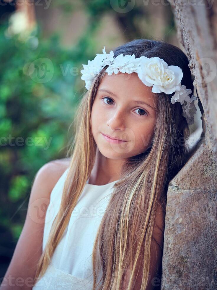 Cute girl in wreath sitting and looking at camera while leaning photo