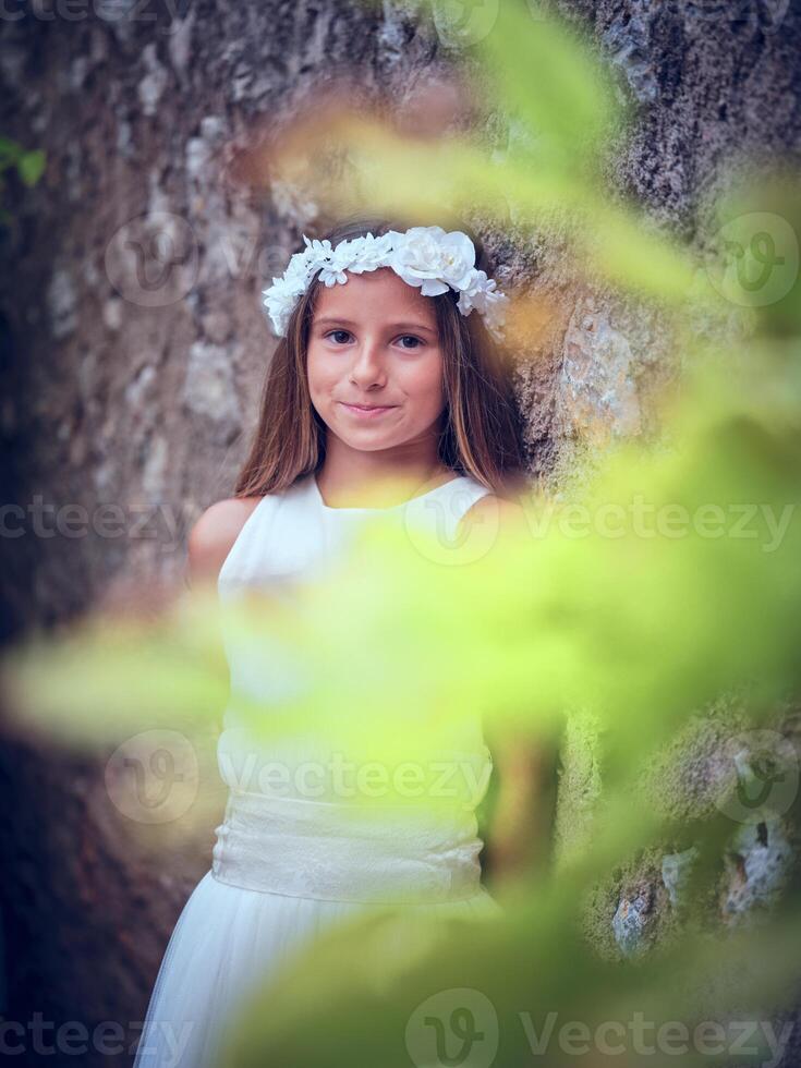 Smiling girl in white flower wreath standing near tree photo