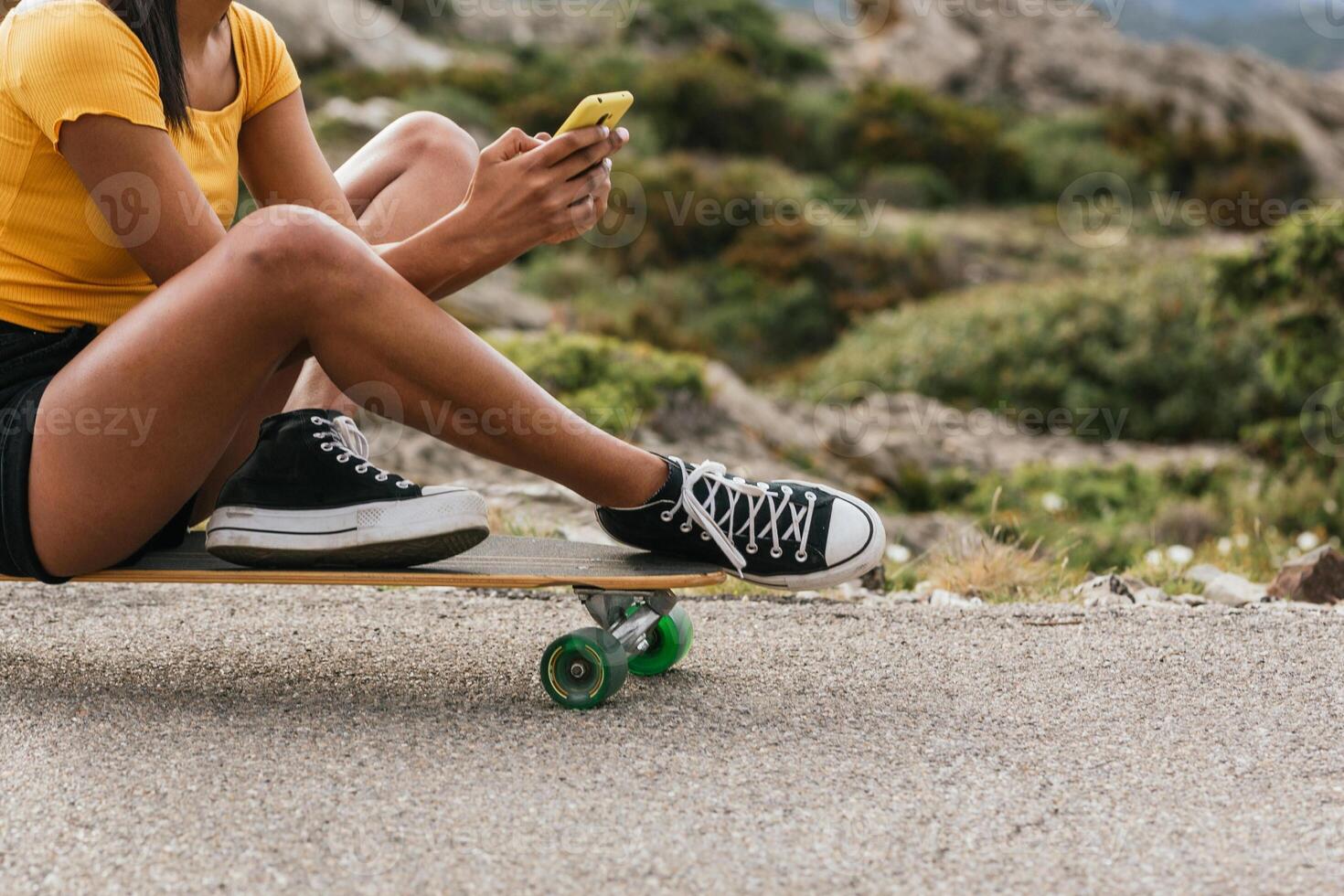 Anonymous woman using mobile phone while sitting on longboard photo