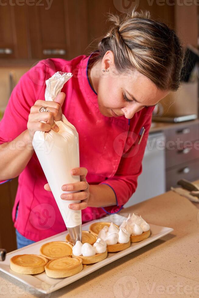 Chef making decorations of whipped cream on tarts photo
