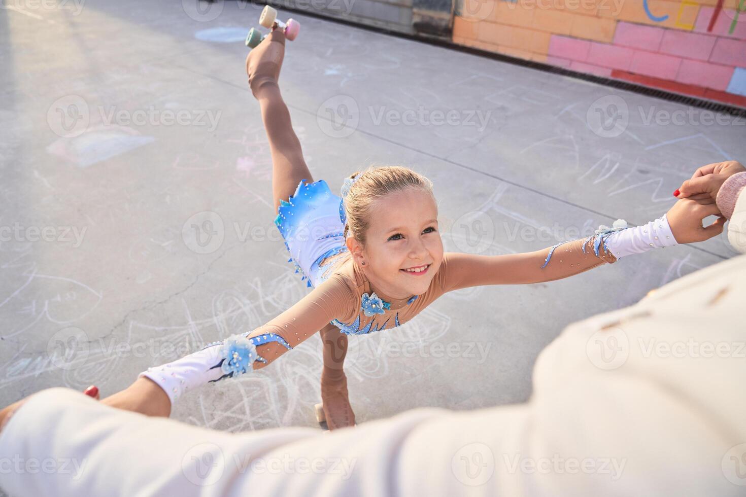 Cheerful girl in roller skates training with faceless trainer photo