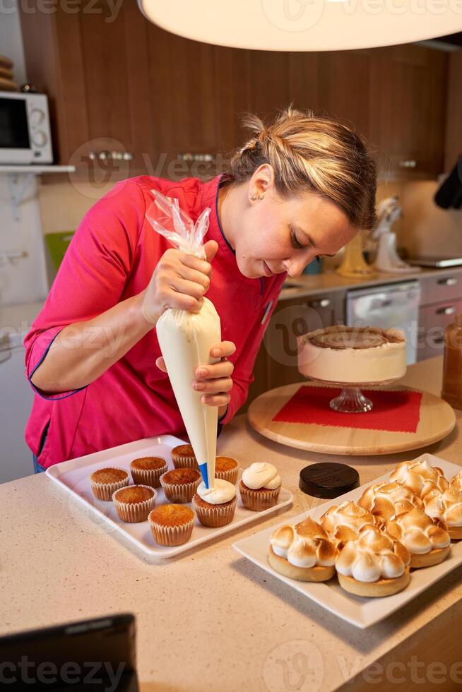 Female confectioner decorating cupcakes using piping bag photo