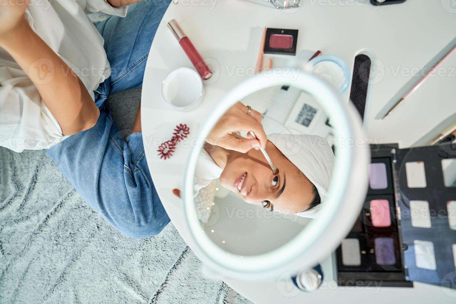 Crop woman doing eyes makeup with brush sitting on floor photo