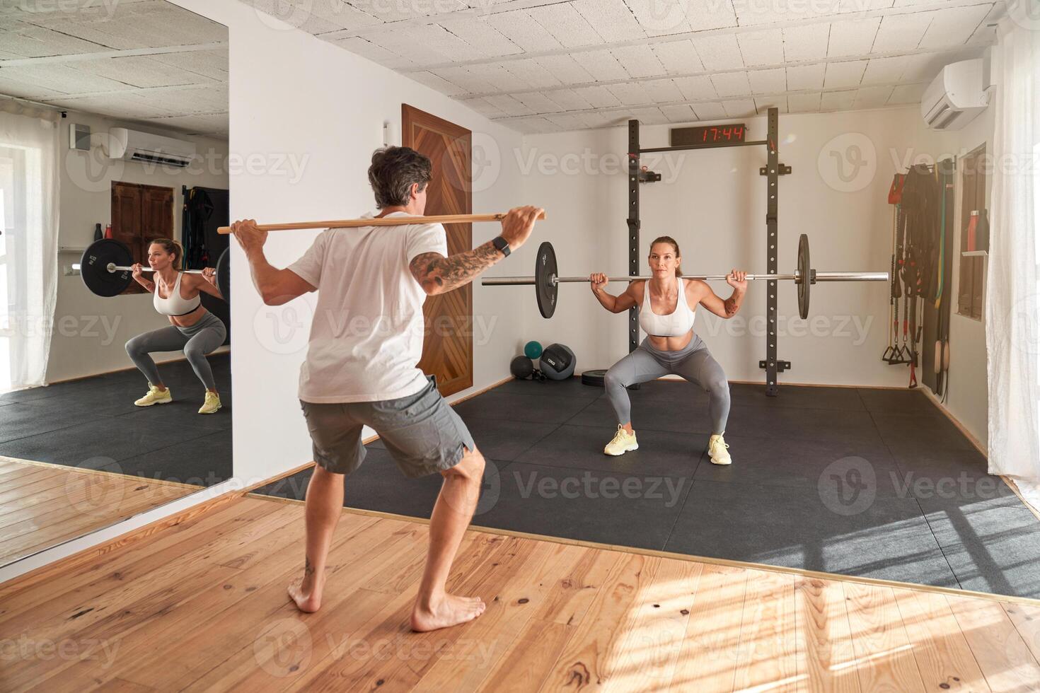 Trainer guiding athlete exercising with barbell in gym photo