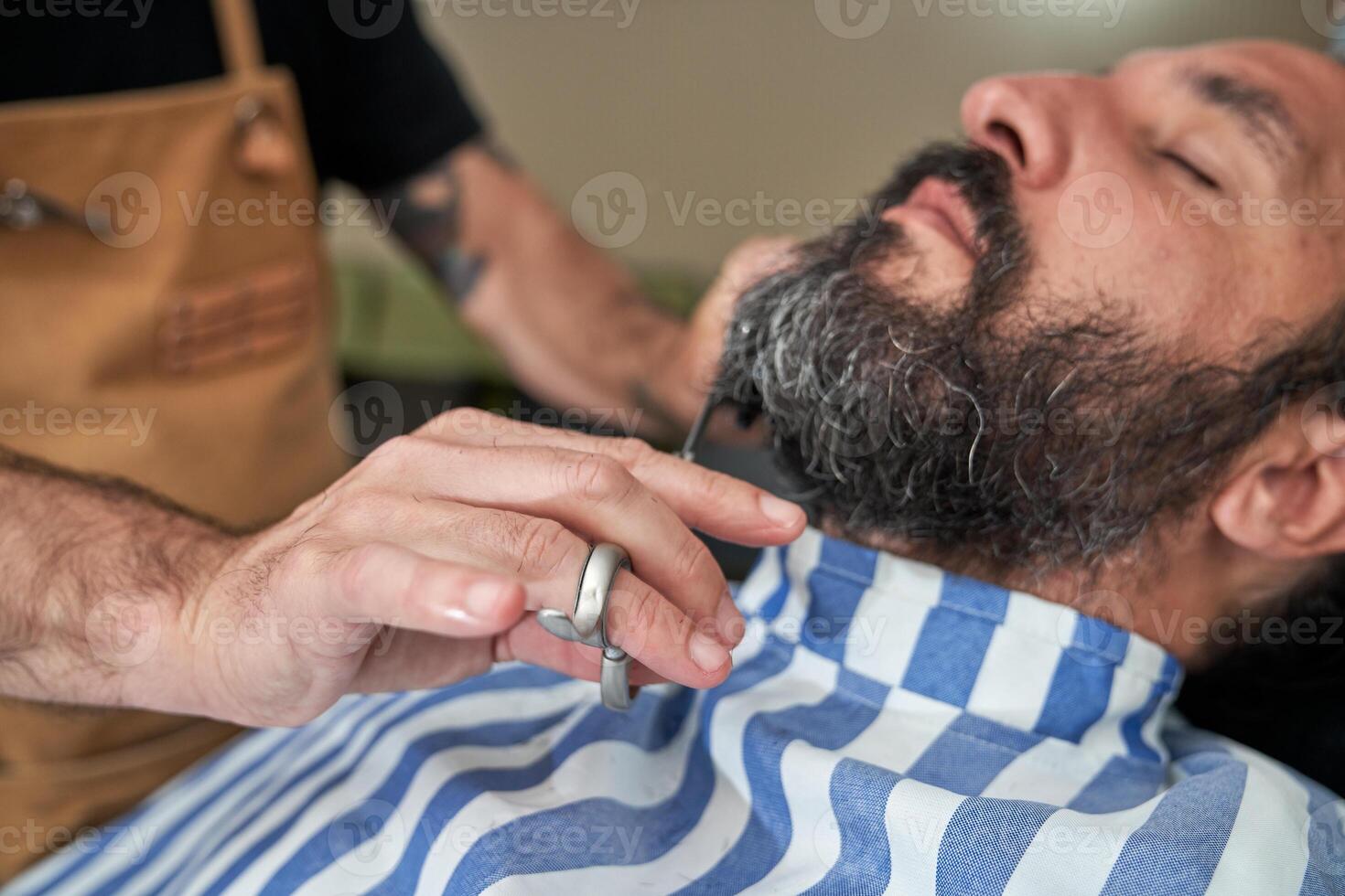 Crop hairdresser cutting beard of man in barbershop photo