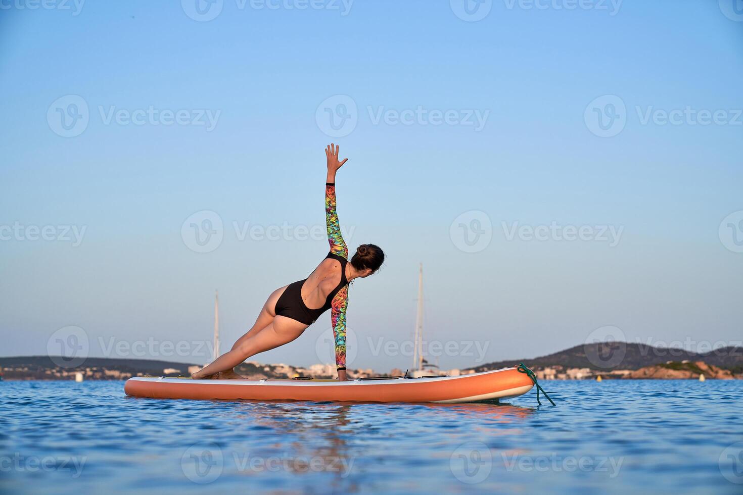 Unrecognizable woman practicing yoga in Side Plank on paddleboar photo