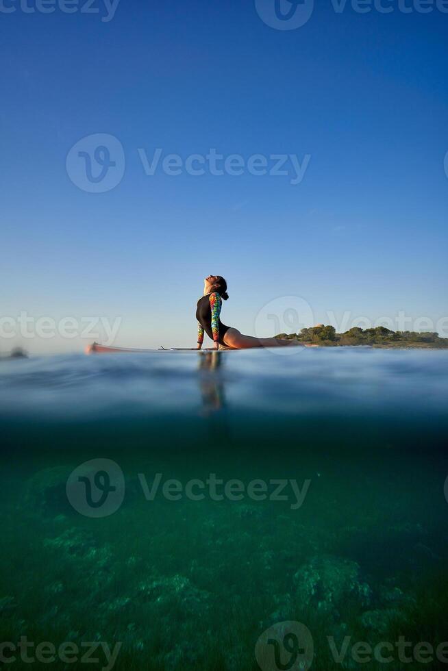 Unrecognizable woman practicing yoga in Cobra pose on SUP board photo