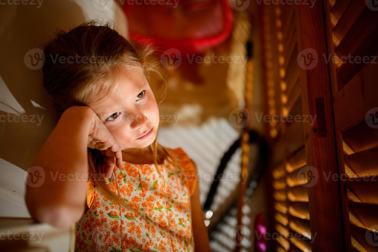 Bored girl leaning on hand against shutters in sunbeams photo