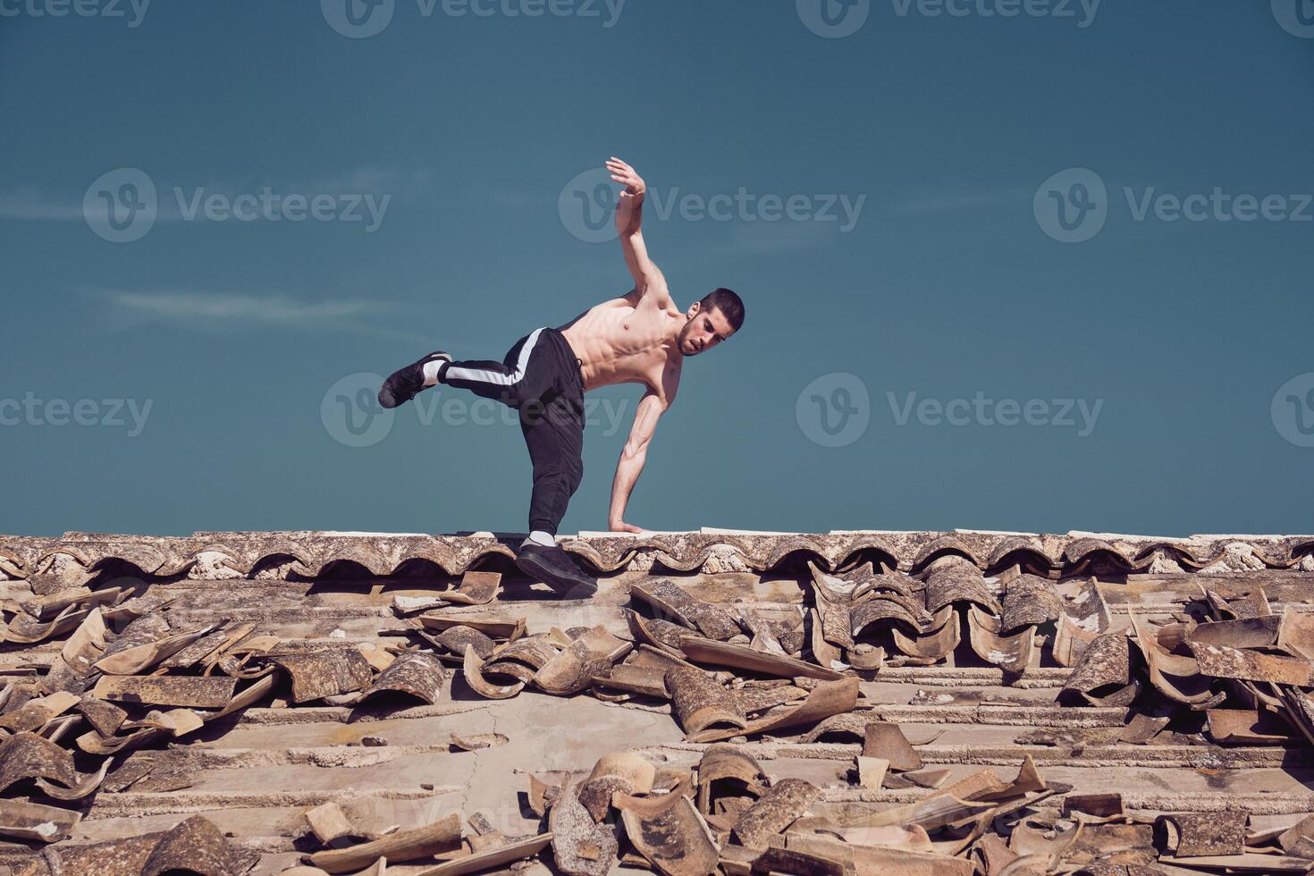 Athletic man performing handstand rotation while dancing breakdance on roof photo