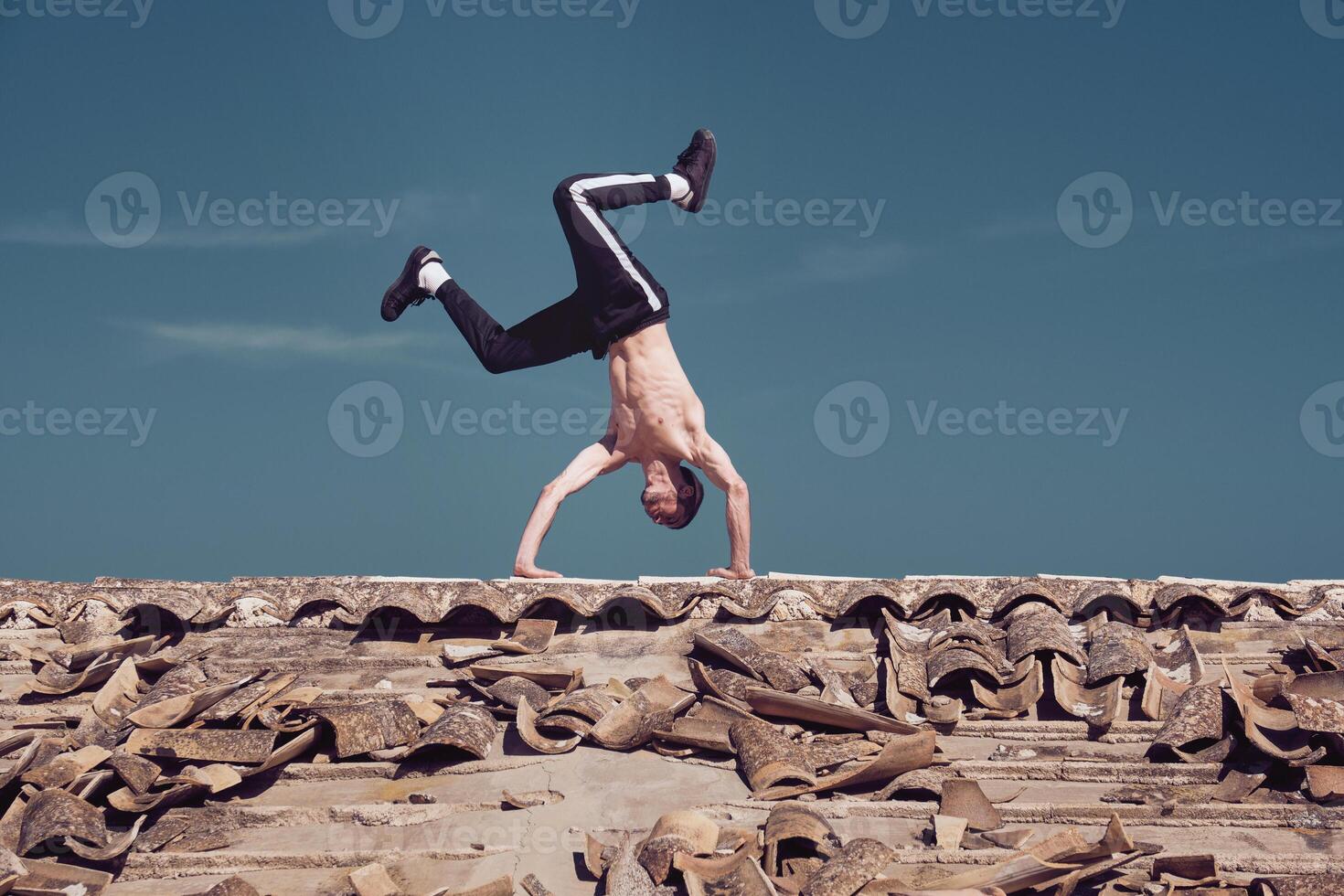 Flexible man performing tow handstand element of breakdance on rooftop photo