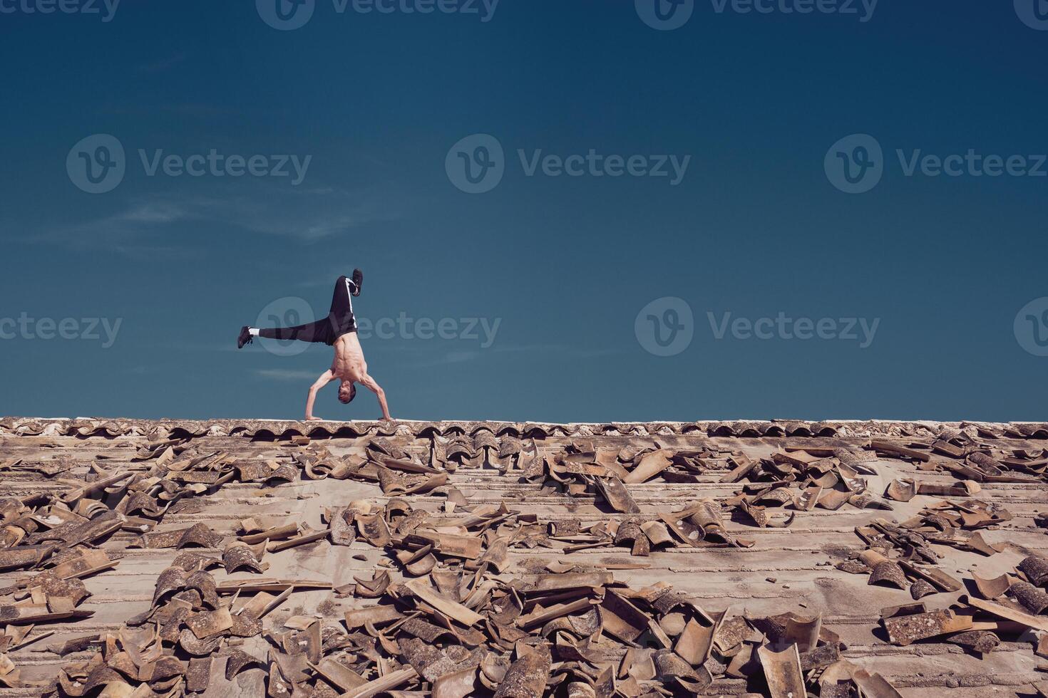 Unrecognizable man performing handstand element of freestyle dance on roof photo