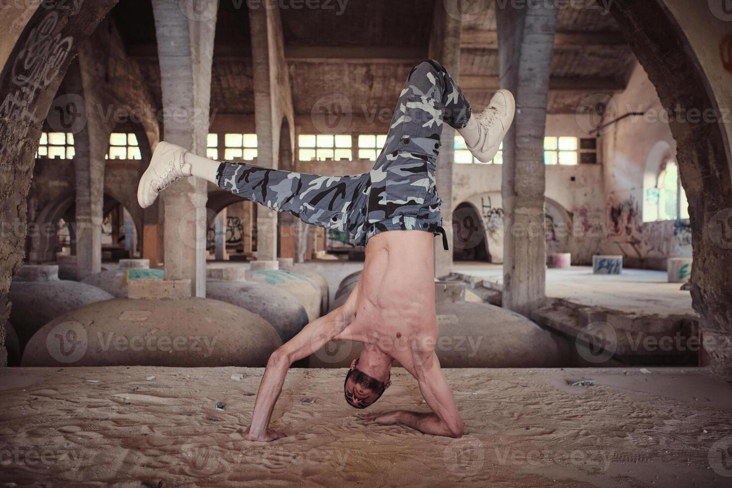 Muscular man performing cricket movement of breakdance in abandoned building photo