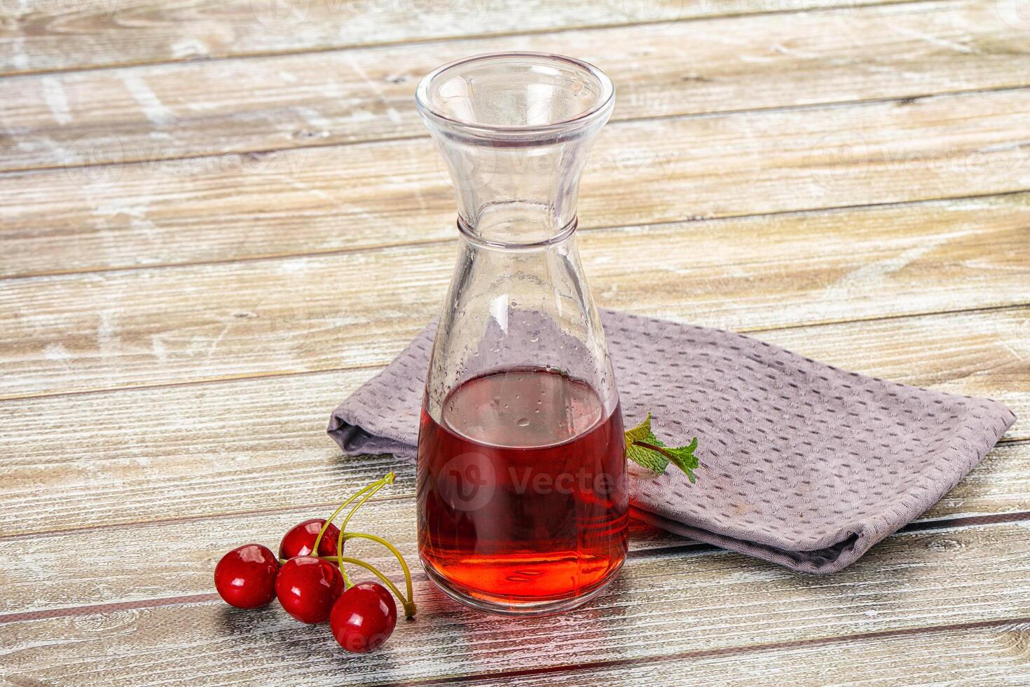 A glass bottle with red liquid and cherries photo