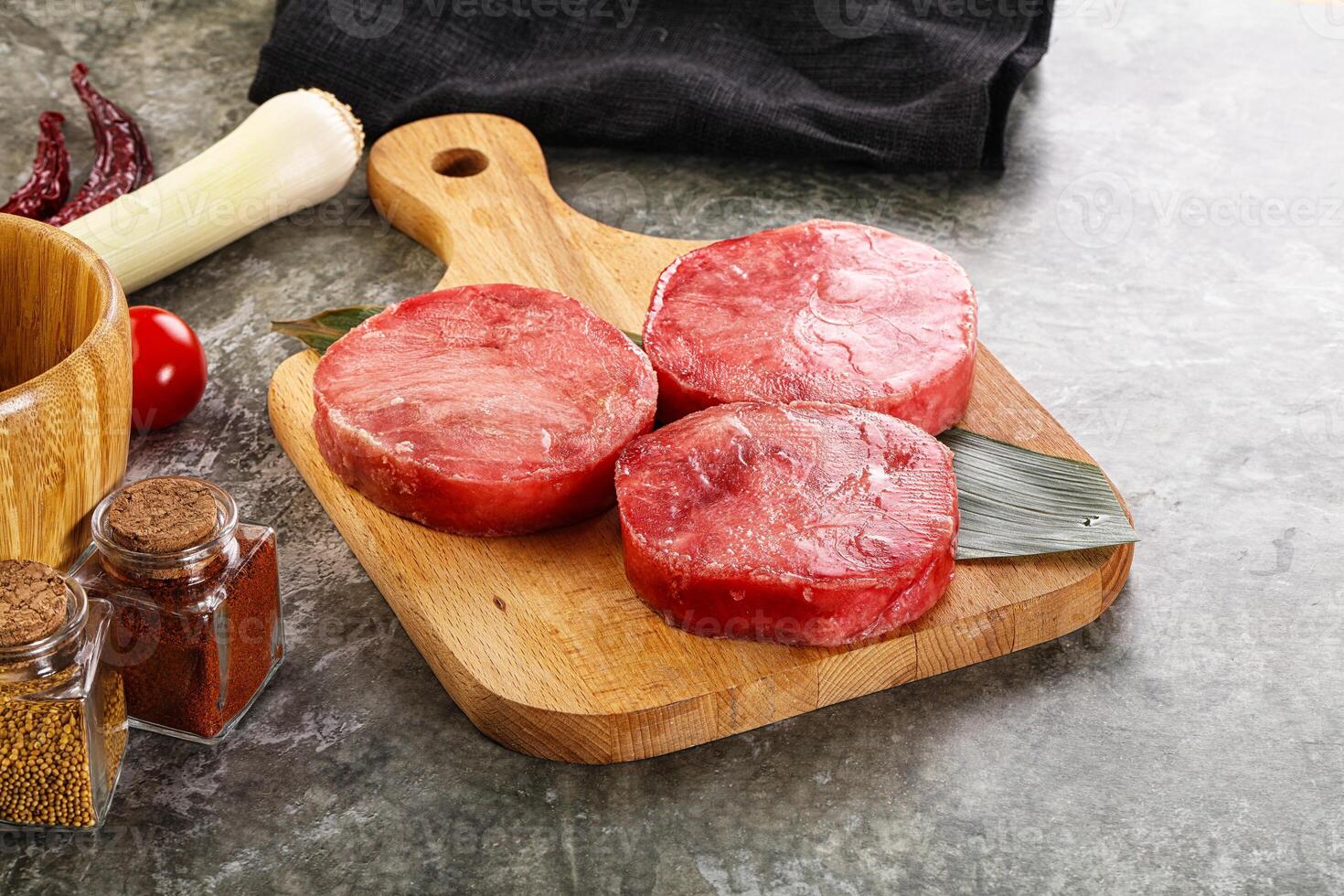 Three raw beef steaks on a cutting board next to spices and other ingredients photo