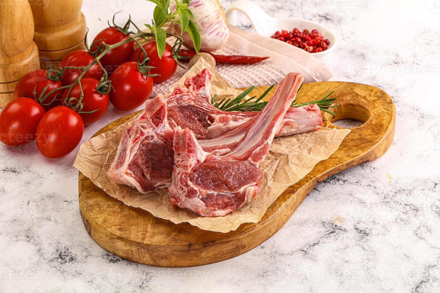 Raw lamb chops on a cutting board with tomatoes and herbs photo