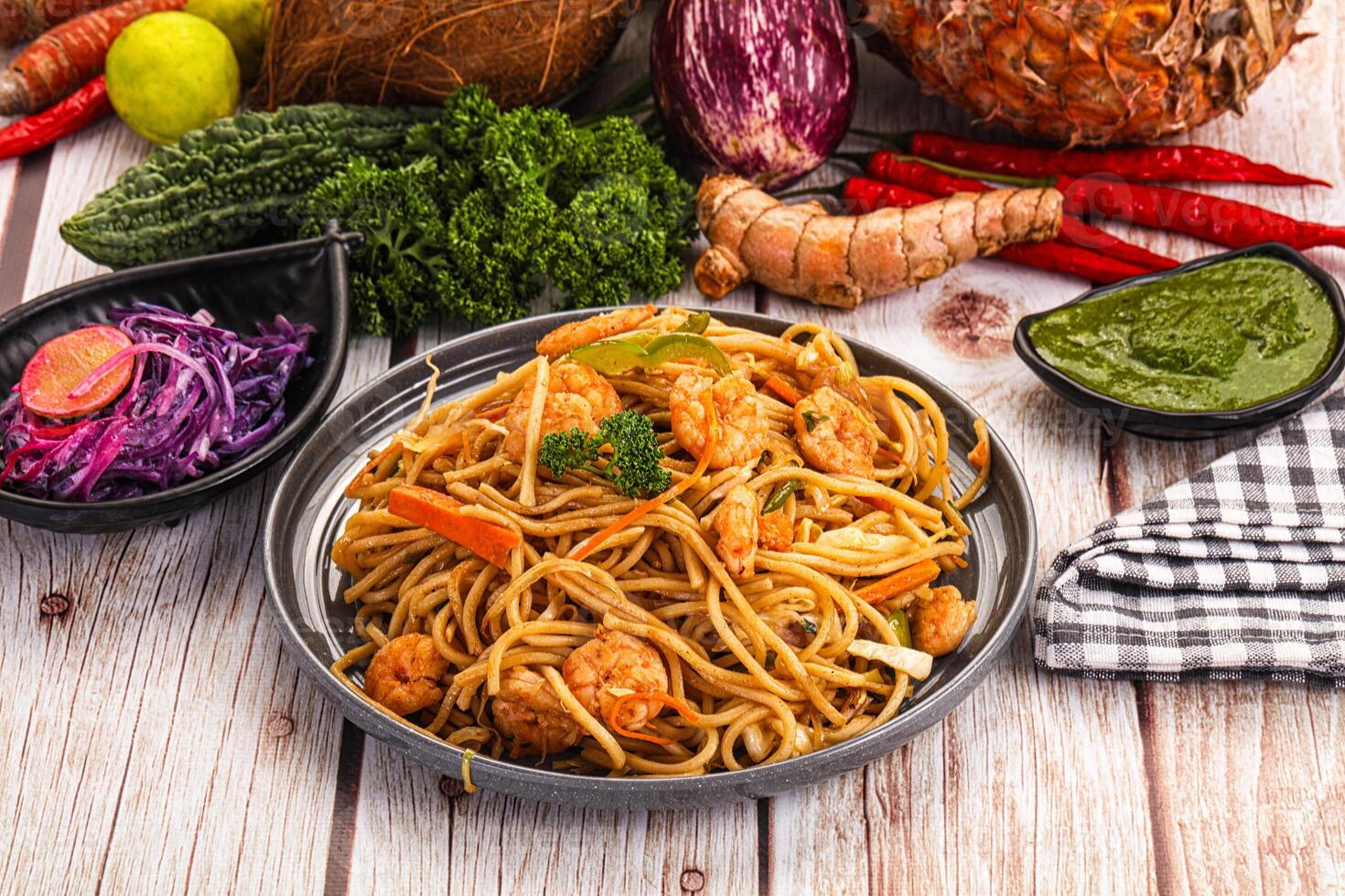 A plate of noodles, vegetables and other food on a wooden table photo