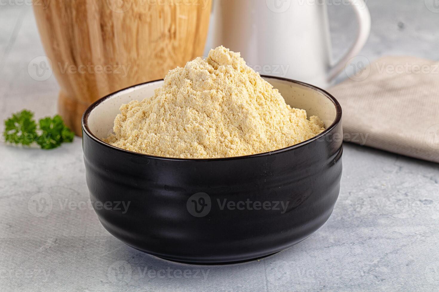 A bowl of yellow powder next to a cup of milk photo